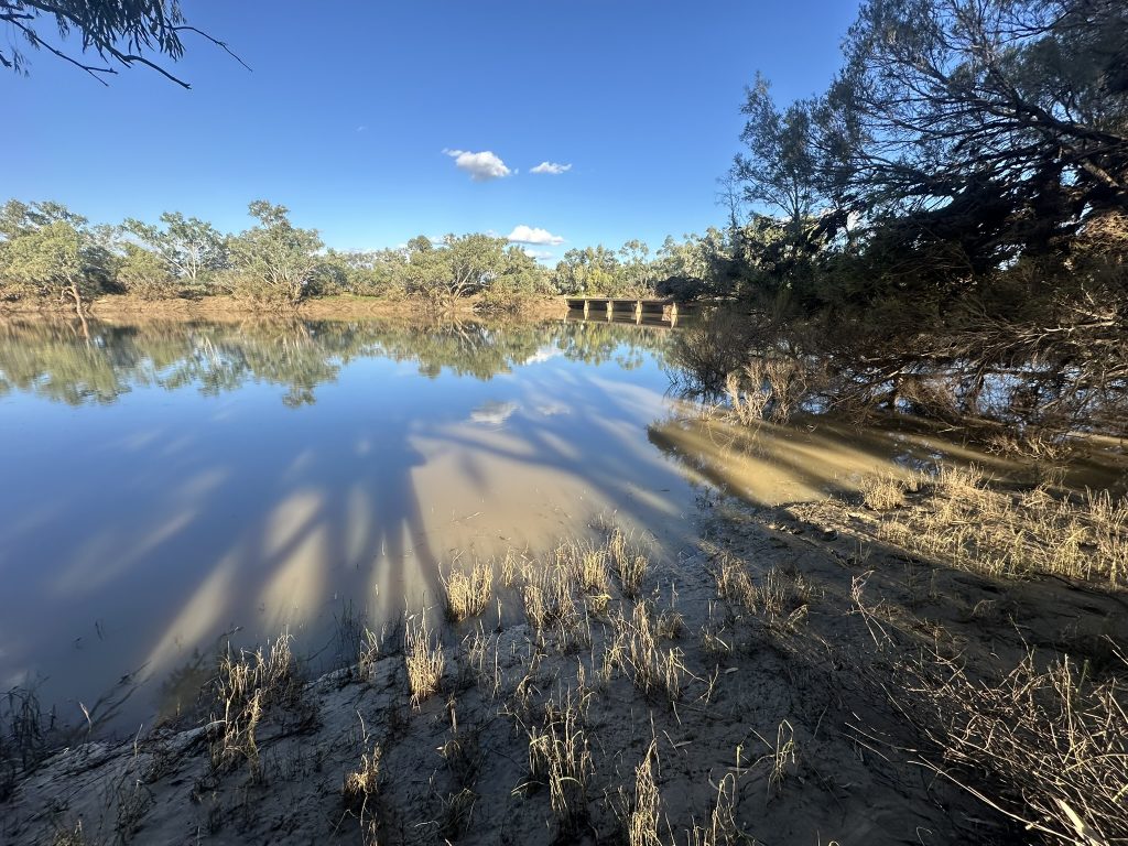 A muddy, depleted creek bed and a nearby bridge that was once submerged under floodwater.