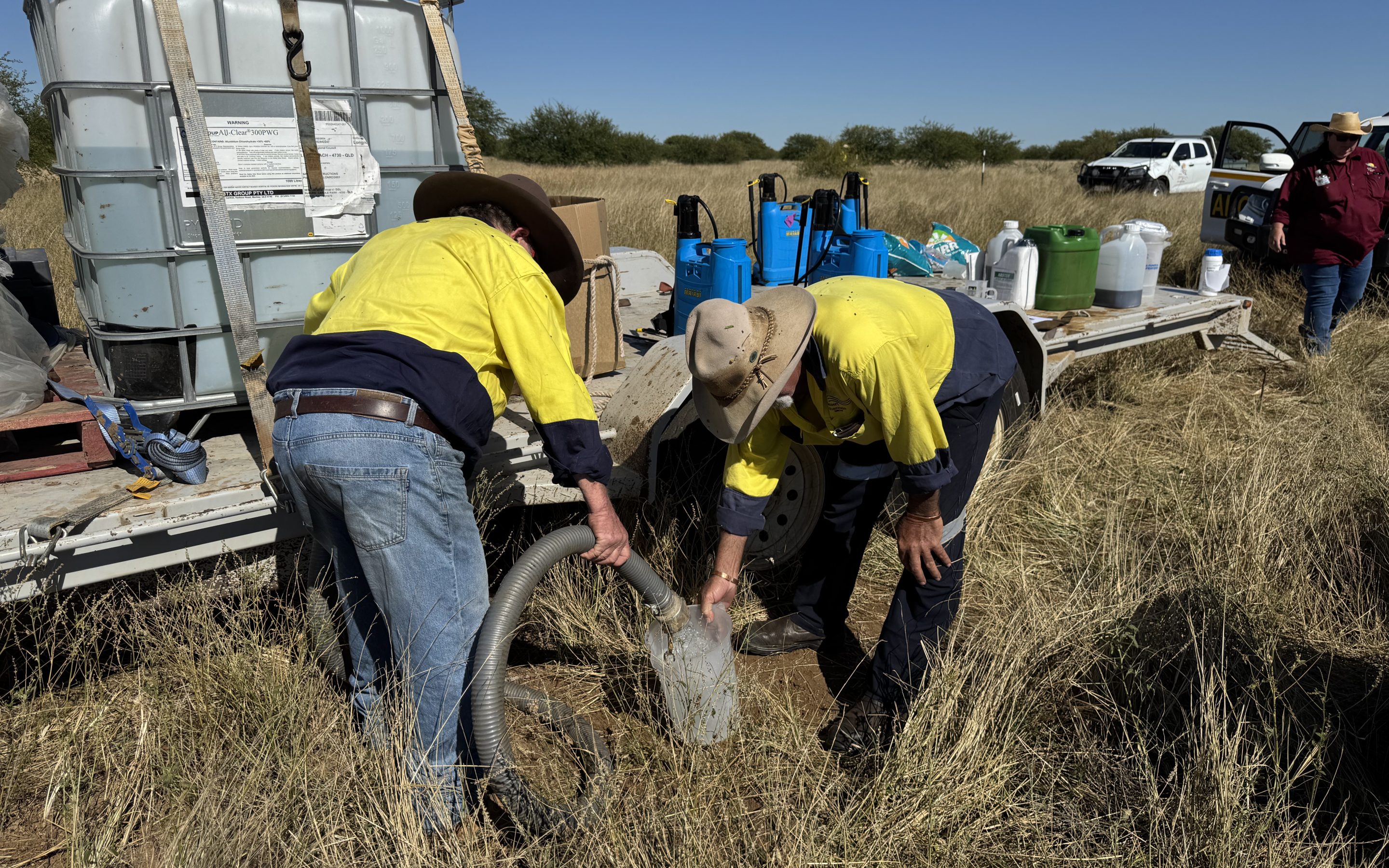 Envu (4) Two blokes in workshirts pore a pipe pumping water into a jug mixed with herbicide chemical.