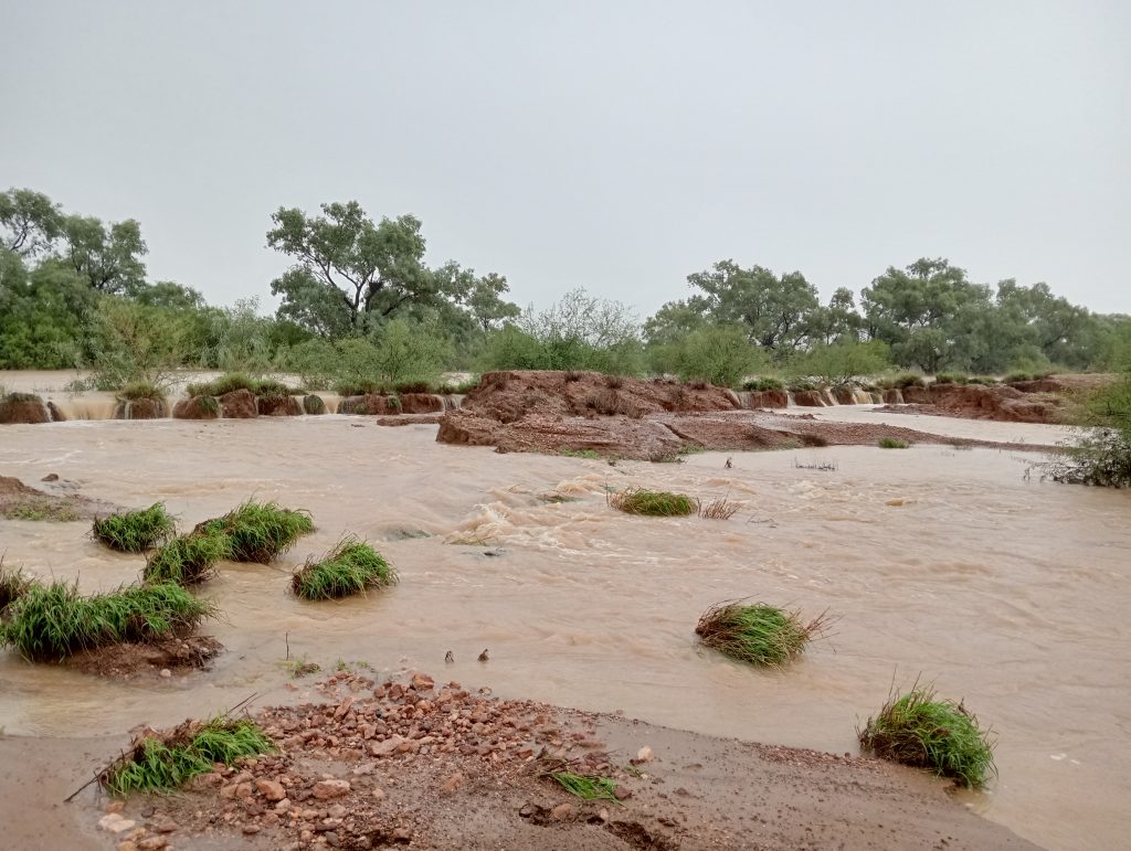 A sheet of rapidly flowing floodwater rips up clay banks, as more fain falls from above.