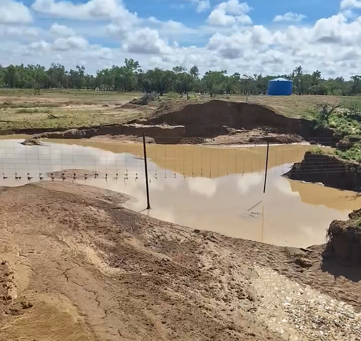 The bank of a waterhole collapses, leaving a fenceline hanging in the air.