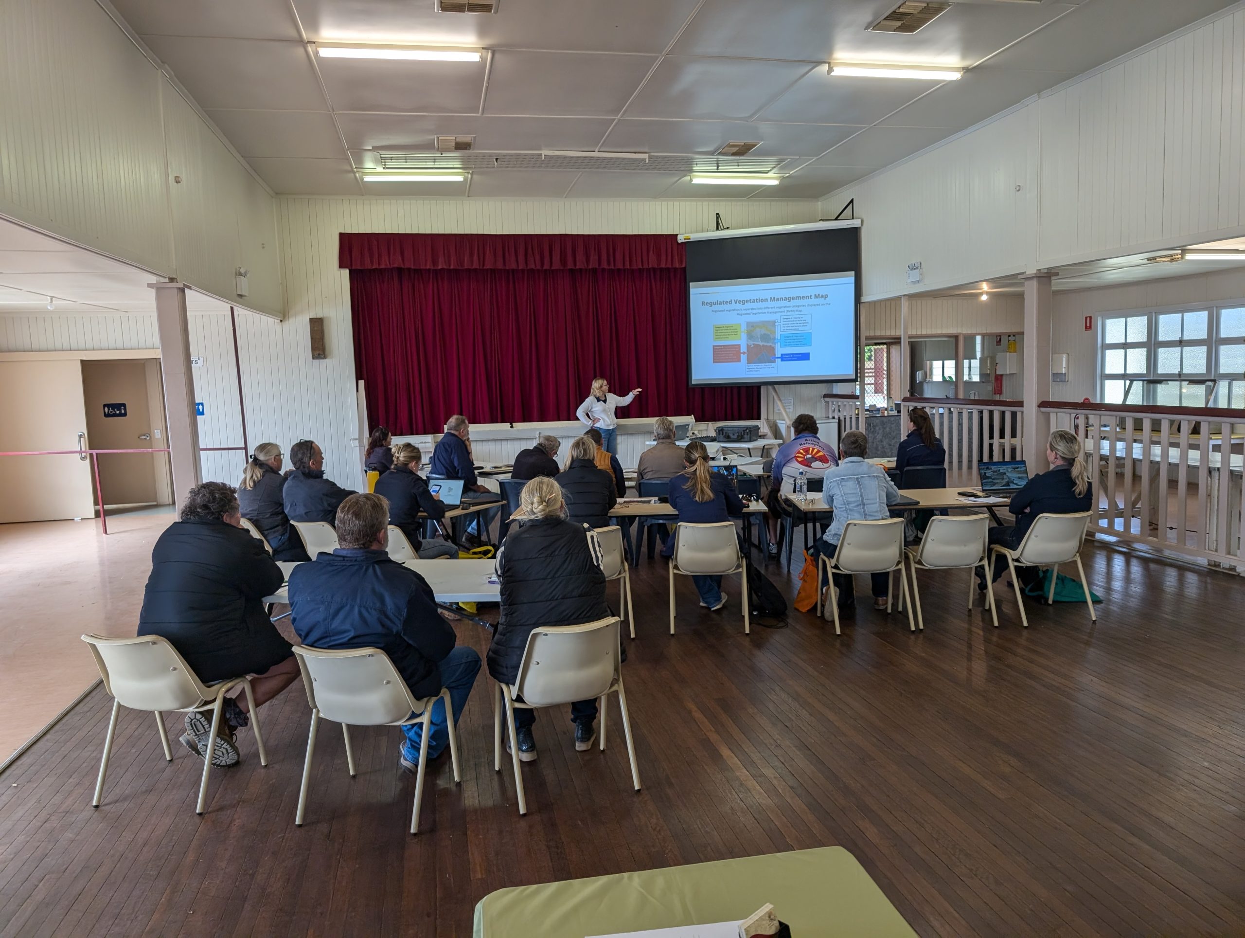 Jericho Vege Management Workshop (12) A crowd of landholders and contractors attend a workshop in an old-style town hall. On the project screen is a slide titled "Regulated Vegetation Map".