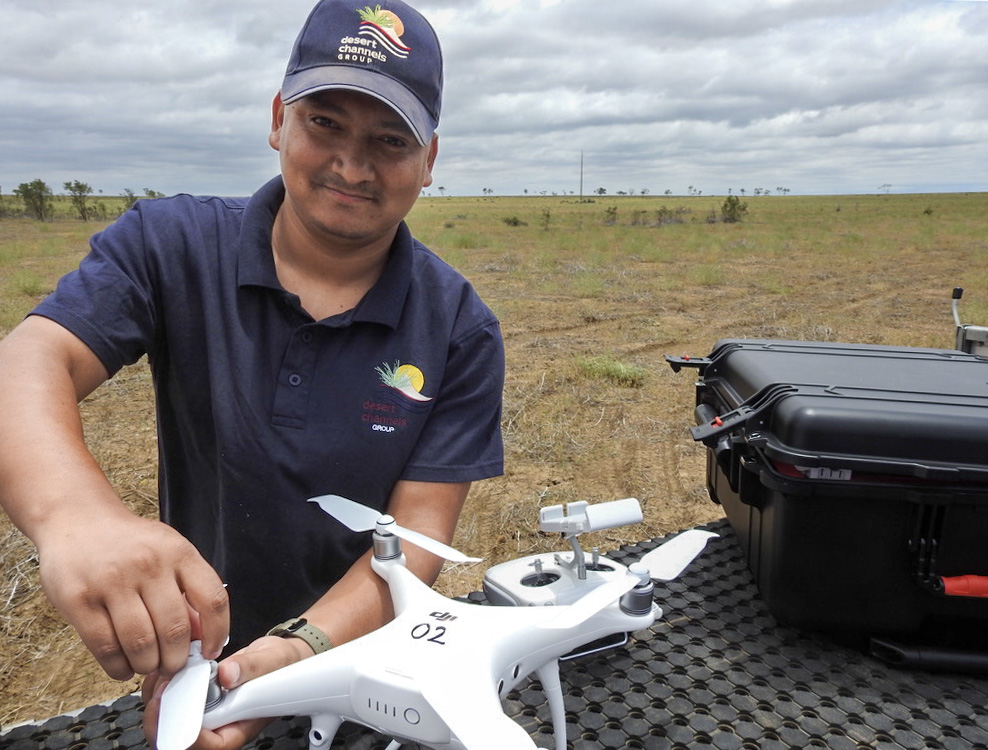 A man in a DCQ cap inspects a brand new white drone in Outback Queensland.