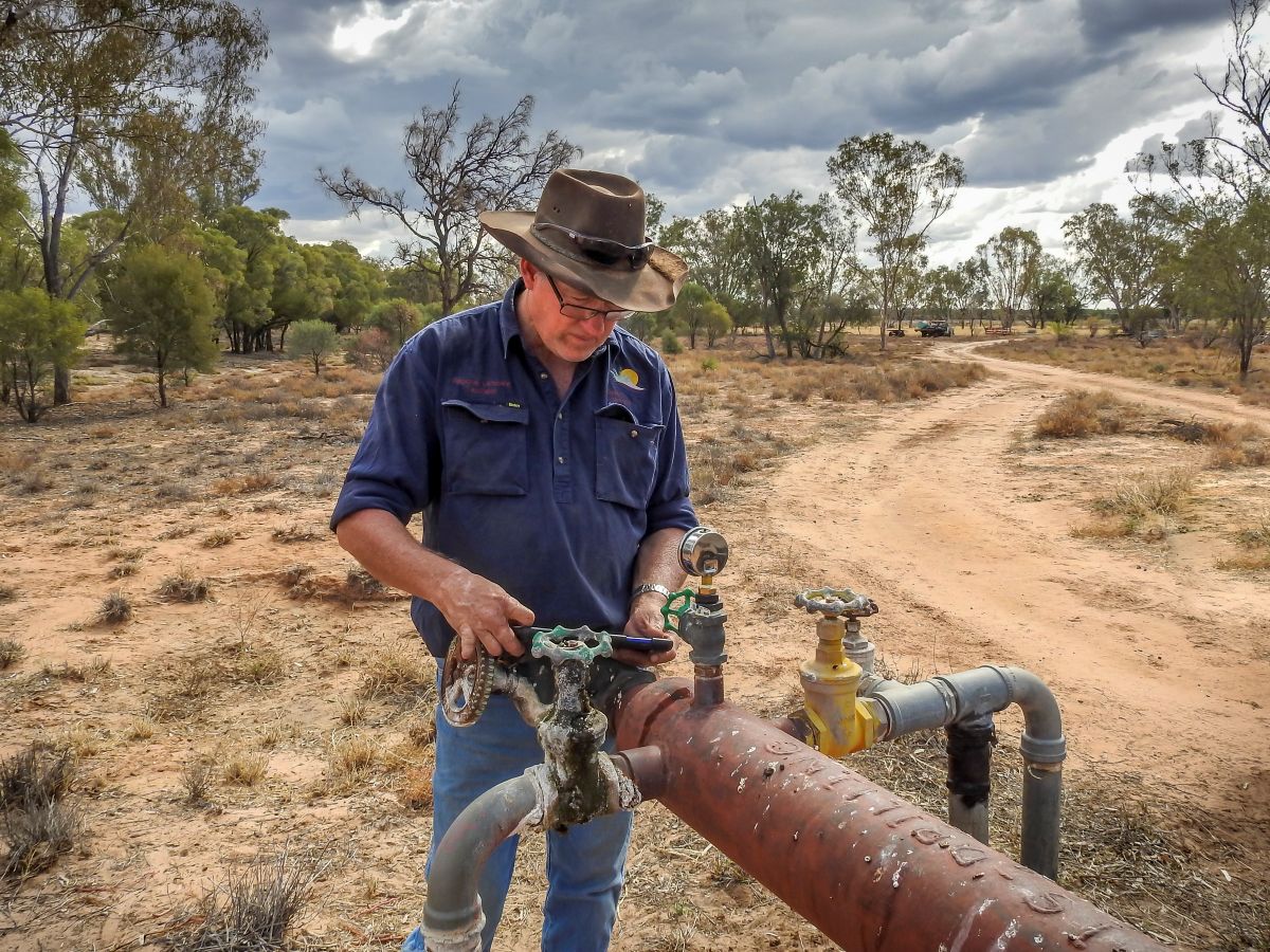 A DCQ staff member uses a small device to inspect a capped groundwater bore on a property in Western Queensland.